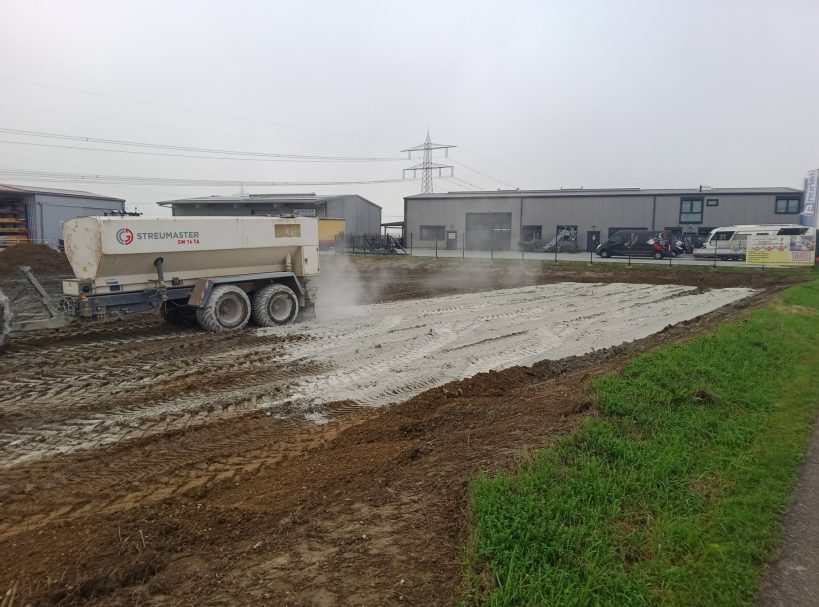 Bodenstabilisierung durch Kalken Baustelle mit einem Lkw, der frischen Beton auf eine unebene Fläche verteilt.