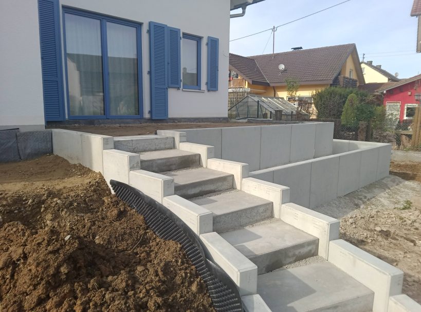 Steintreppe und L-Steine Treppen aus Beton führen zu einem Haus mit blauen Fensterläden und einer Terrasse.