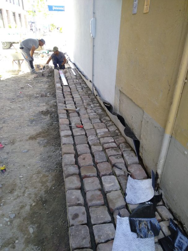Sanierung Pflastersteine Fußweg Altstadt Arbeiter verlegen Pflastersteine auf einem Gehweg neben einer Hauswand.