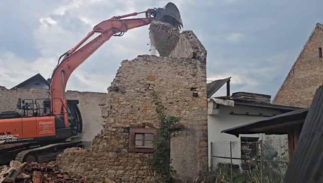 Abriss alter Hauswand Ein Bagger reißt eine teilweise abgerissene Steinmauer in einem Gebäude ab.