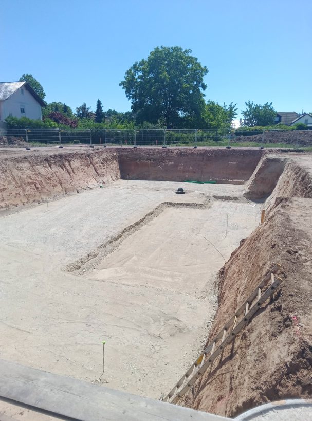 Einbau Tragschicht Baustelle mit ausgehobenem Erdreich für ein Fundament unter strahlend blauem Himmel.