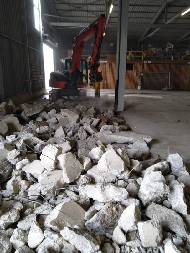 Betonspitzarbeiten Bauschutt liegt auf dem Boden, ein Bagger arbeitet im Hintergrund.