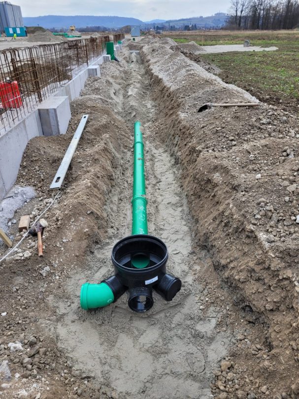 Entwässerungsleitung Grüne Abwasserrohre liegen in einem ausgehobenen Graben auf unbefestigtem Boden.