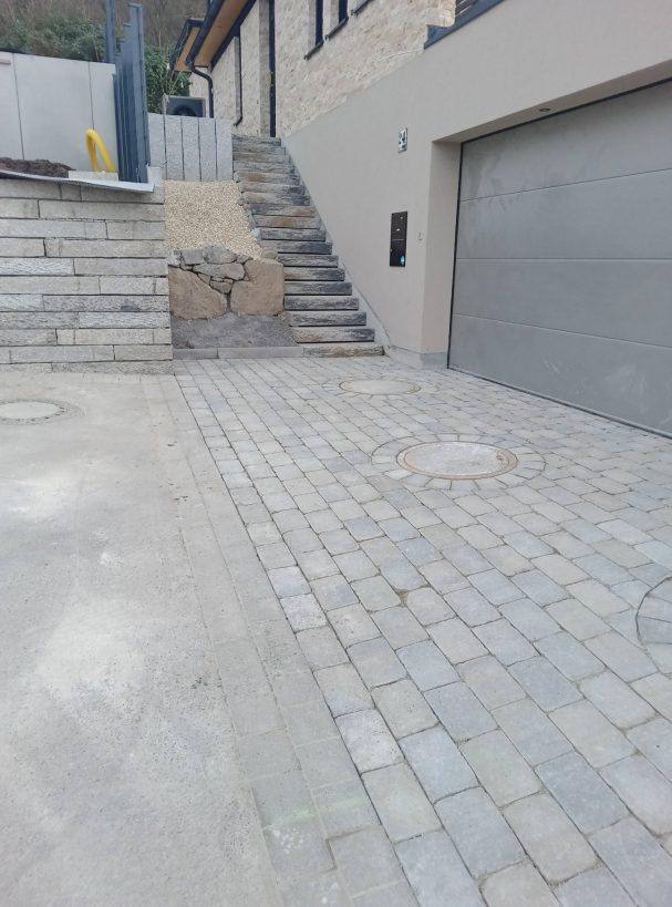Gepflasterte Hofeinfahrt Verklinkerte Einfahrt mit Steinstufen und Garage, modernes Wohnhaus im Hintergrund.