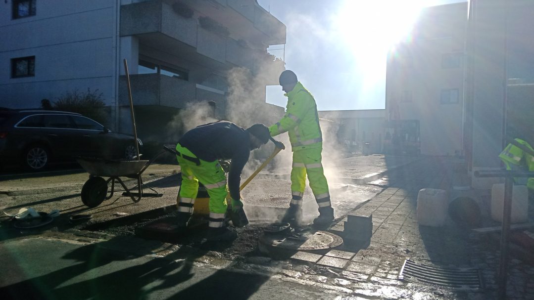 Grundstückserschließung Arbeiter in leuchtend gelben Sicherheitsanzügen reparieren den Straßenbelag.