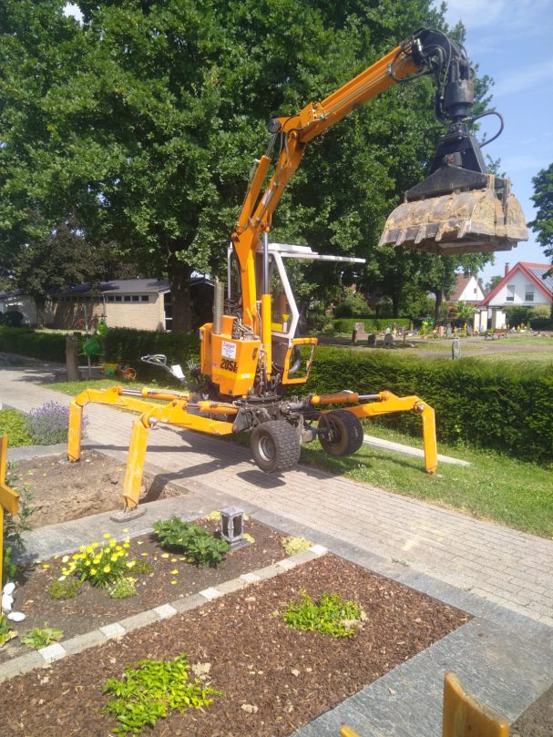 Friedhofs-Kompaktbagger Gelber Bagger mit Greifarm hebt eine Last in einer Gartenlandschaft.