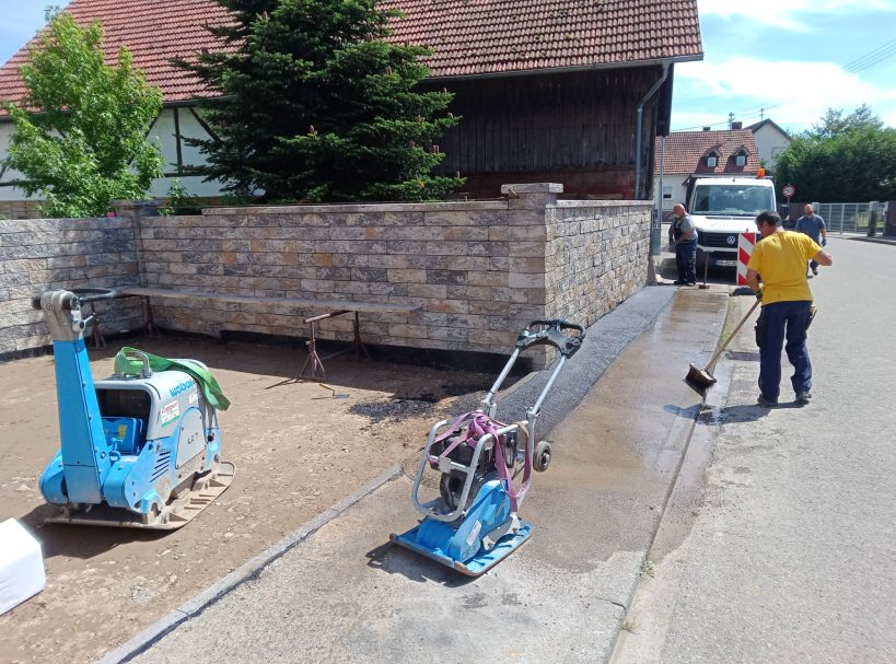 Trockenmauerwerk Bauarbeiter mit Maschinen und Lkw auf einer Baustelle neben einem gemauerten Zaun.