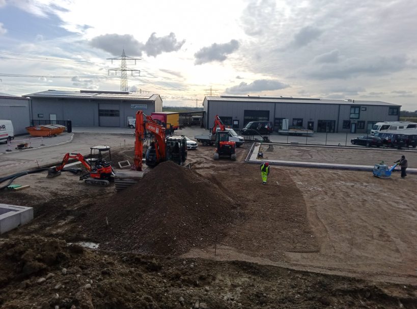Baufeldvorbereitung Baustelle mit Maschinen, Erde bewegt, und Arbeitern in einem Gewerbegebiet.