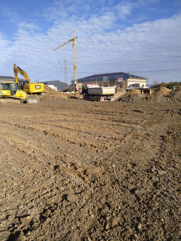 Planierarbeiten auf einem Baufeld Baufeld mit schwerem Gerät, unbefestigtem Boden und Kränen im Hintergrund.