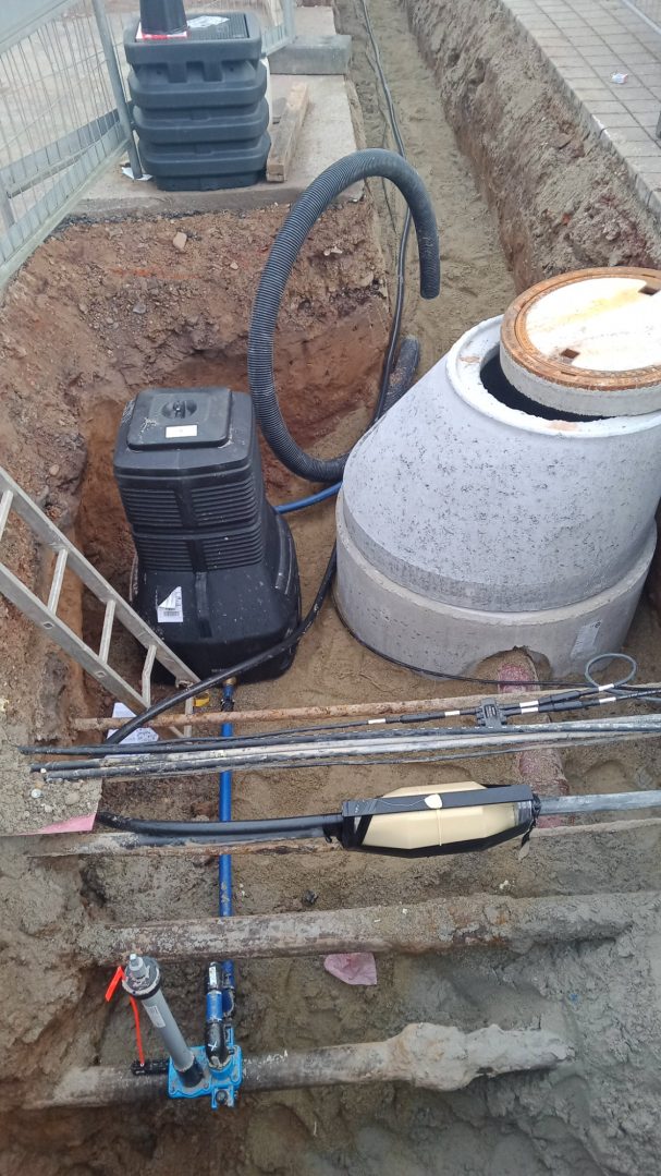 Schachtbauwerk Graben mit einem Betonbehälter und einem schwarzen Gerät, Rohrleitungen und einer Leiter.